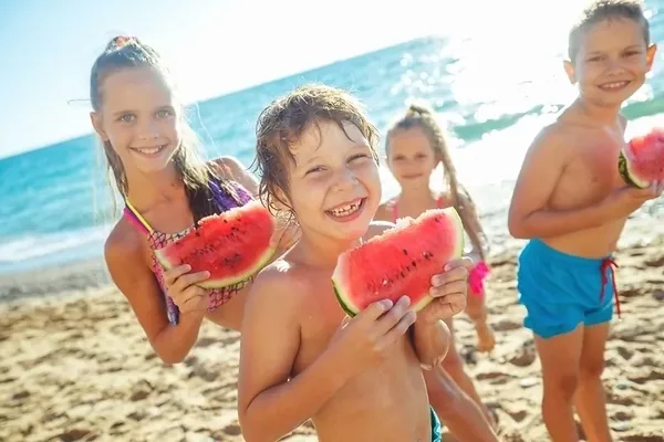 Dzieci jedzą kawałki arbuza na piaszczystej plaży
