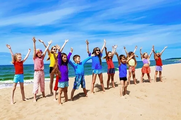 Grupa uczestników kolonii z uniesionymi rękami na nadmorskiej plaży