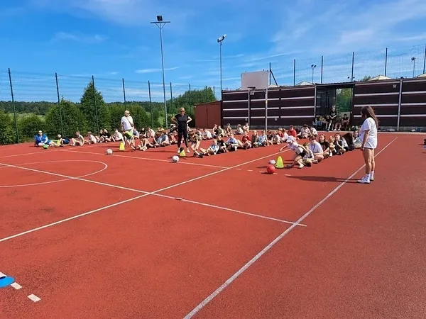 Dzieci podczas konkurencji sportowych na czerwonej nawierzchni boiska