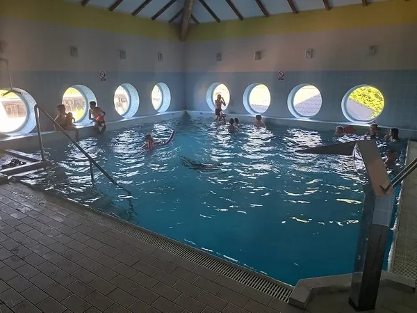 Kryty basen ośrodka z okrągłymi oknami i uczestnikami w wodzie