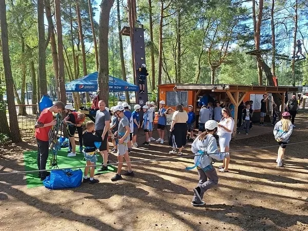 Grupa dzieci przy stanowiskach parku linowego w sosnowym lesie