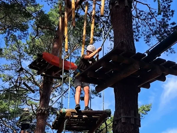 Dziecko w kasku na drewnianej platformie wysoko w parku linowym