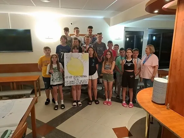 Uczestnicy kolonii pokazują plakat swojej grupy w sali ośrodka