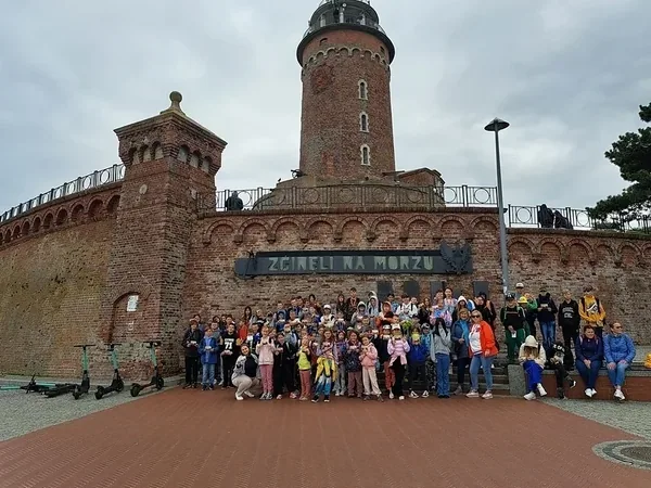 Grupa uczestników wycieczki przed ceglaną latarnią morską