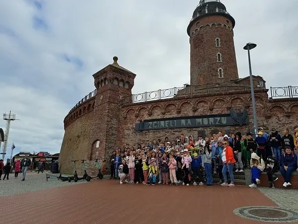 Koloniści pozują u stóp ceglanej latarni morskiej