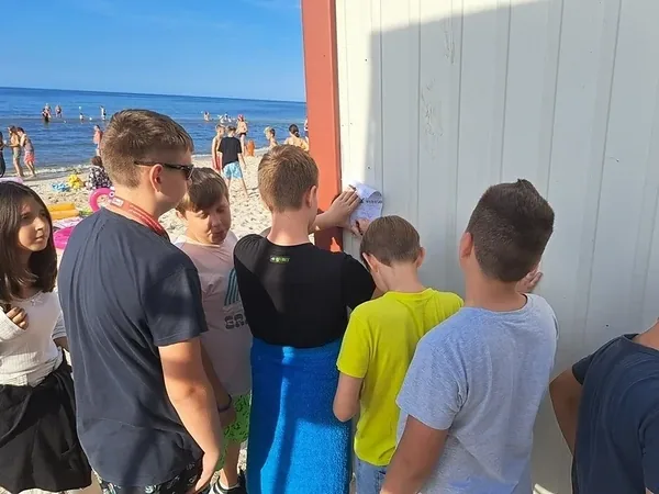 Dzieci zgromadzone przy przejściu na plażę podczas gry terenowej