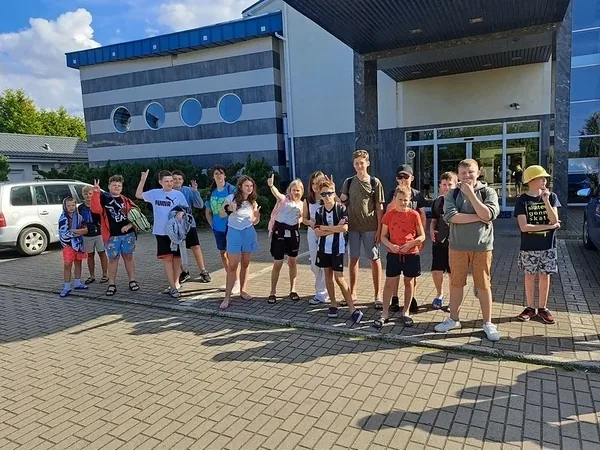 Dzieci z plecakami ustawiają się przed budynkiem ośrodka