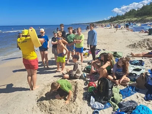 Grupa kolonistów i opiekunów na piaszczystej plaży nad morzem