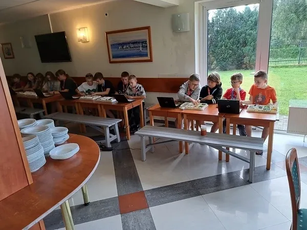 Grupy dzieci przy laptopach i zestawach konstrukcyjnych podczas kolonii