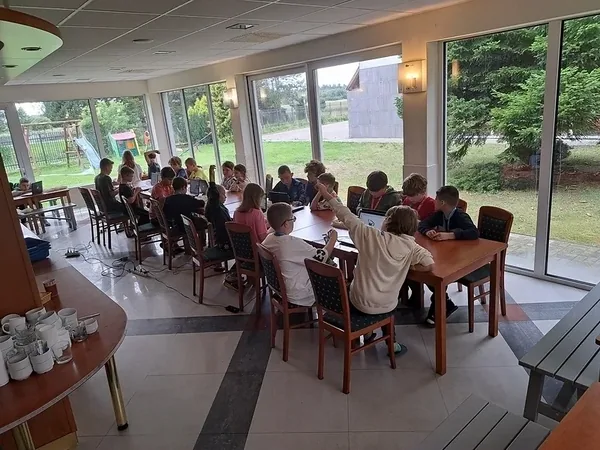 Widok grup kolonistów pracujących przy stołach podczas warsztatów z robotyki