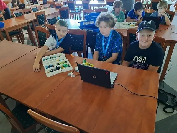 Dzieci wspólnie pracują przy laptopie na warsztatach z robotyki