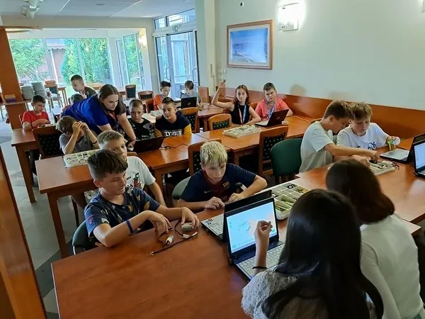 Dzieci w niewielkich grupach budują roboty z klocków w sali ośrodka