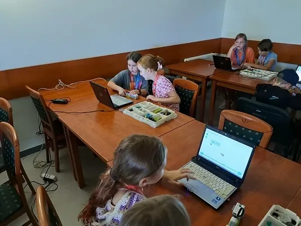 Uczestnicy zajęć z robotyki pracują przy stołach z laptopami